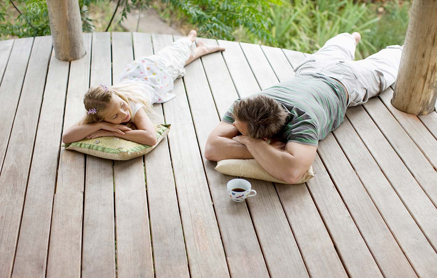 Vater und Tochter liegen nebeneinander auf einer Holzterrasse